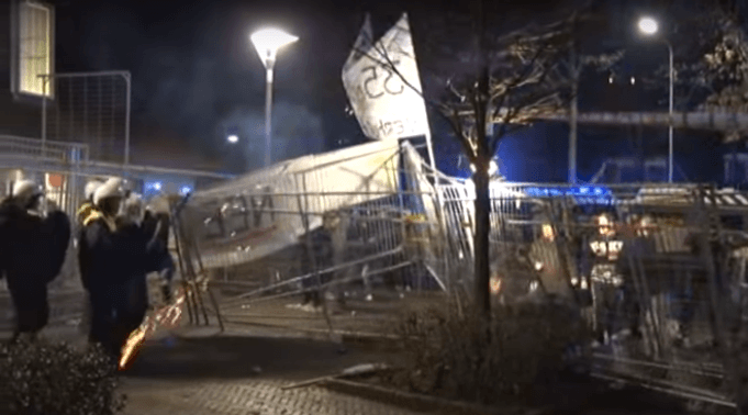 Szene einer Straßenschlacht zwischen 80 gewaltbereiten Demonstranten und Polizisten, die von einem Bauzaun getrennt sind, am Mittwochabend vor dem Rathaus Geldermalsen in den Niederlanden. (Filmausschnitt: Youtube/Omroep Gelderland)